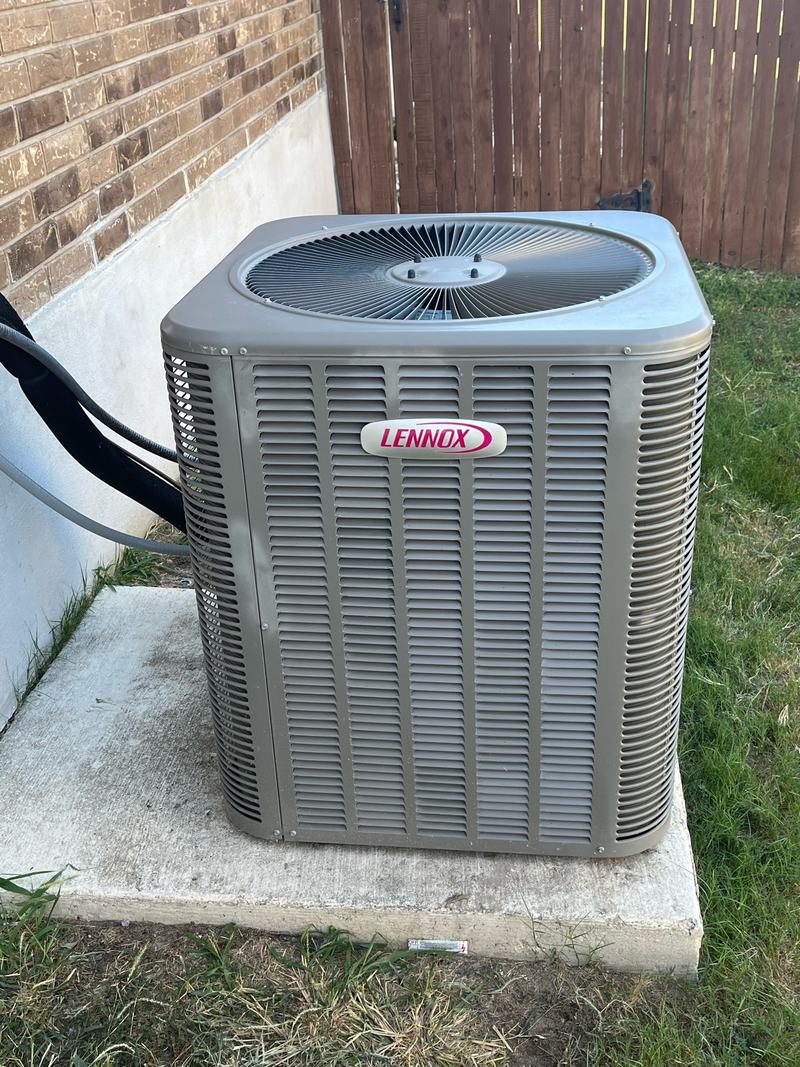 Lennox outdoor condensing unit on a concrete pad beside a brick wall and wood fence