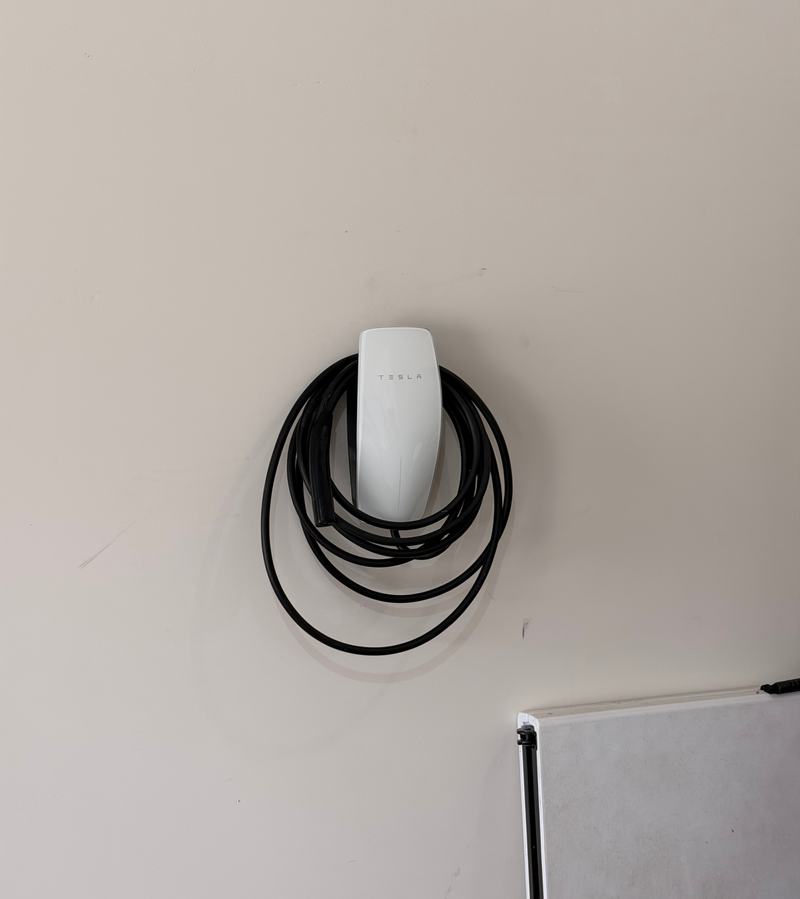 White wall-mounted EV charger with its charging cable coiled around it on a clean garage wall