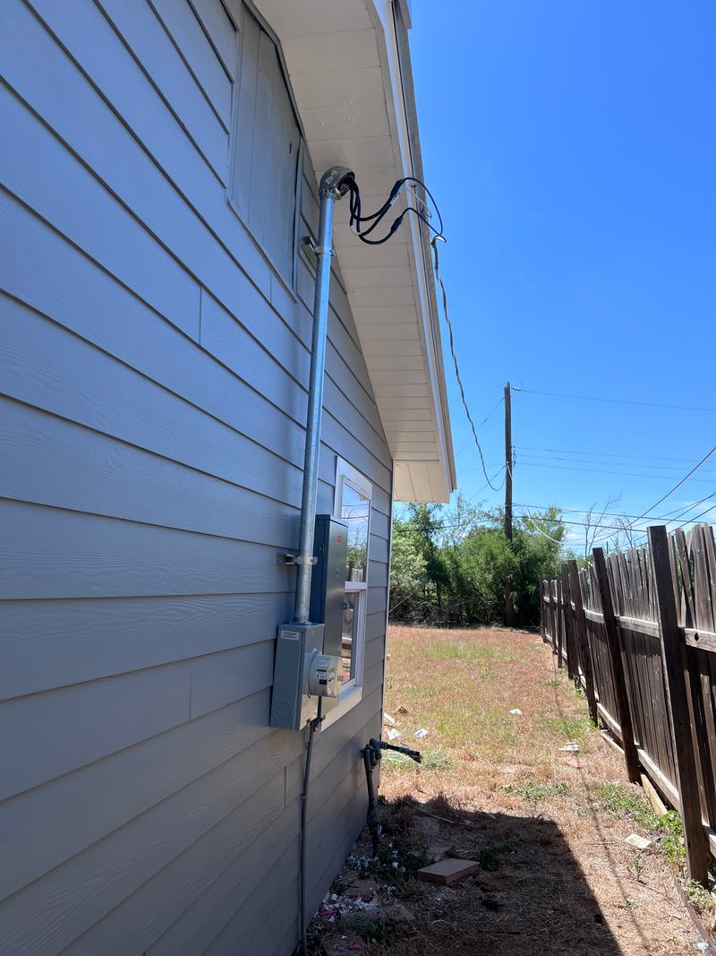 Conduit service mast strapped up the siding toward the eave with the meter base and an enclosure mounted below