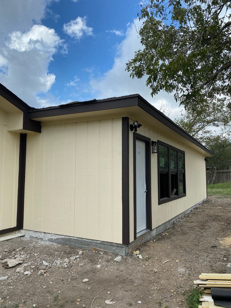New room addition with cream vertical siding, dark trim, a door and a bank of windows