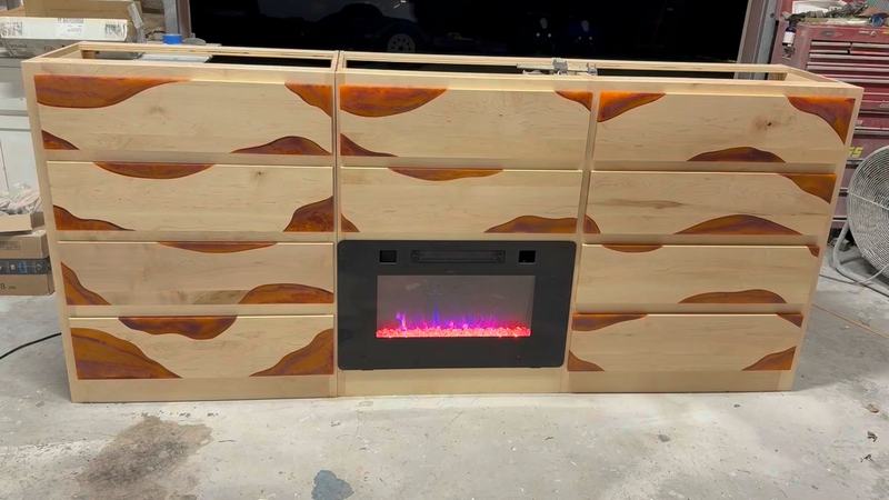 Silent clip of a long light-wood cabinet with resin-filled accents and a lit electric fireplace insert, in the shop