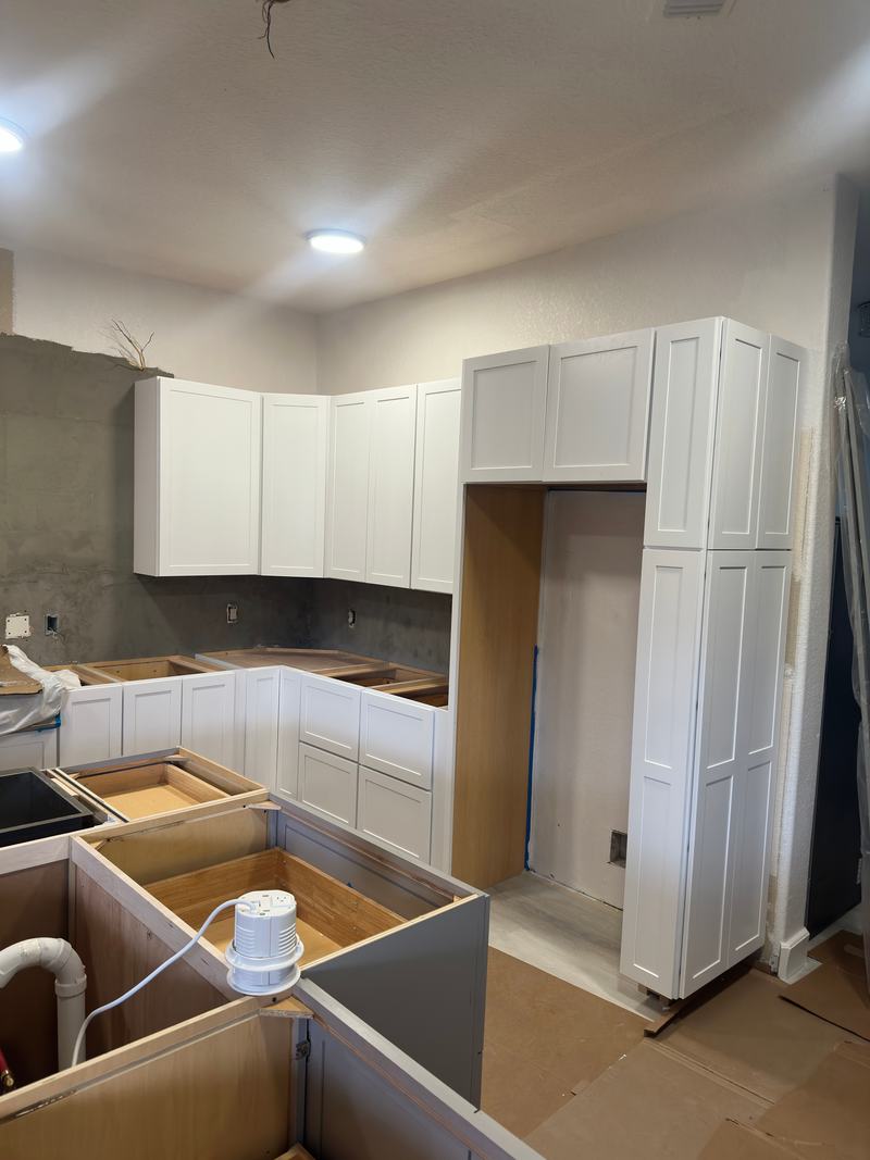White kitchen wall cabinets and pantry tower installed while the base cabinet boxes are still open and untopped