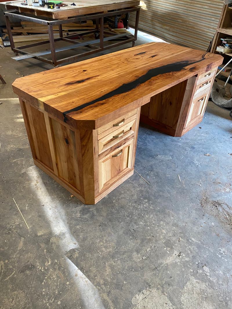 Live-edge hickory desk with a black resin river through the top and two drawer pedestals, photographed in the shop