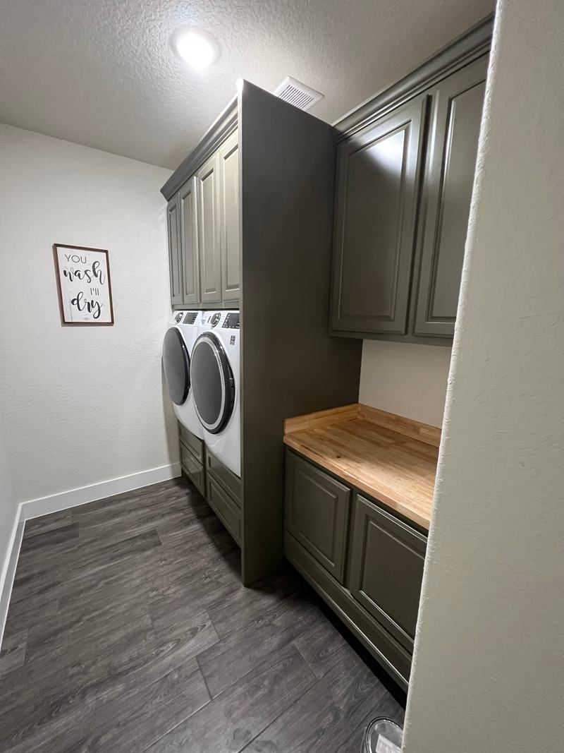Olive green raised-panel laundry built-in with upper cabinets, a tall divider cabinet and a butcher-block folding counter