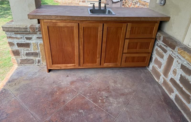 Covered patio cabinet with shaker doors and a three-drawer bank under a poured concrete top with a bar sink