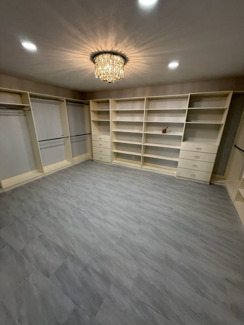Walk-in closet lined with built-in shelving, drawer banks and hanging sections under a crystal ceiling light