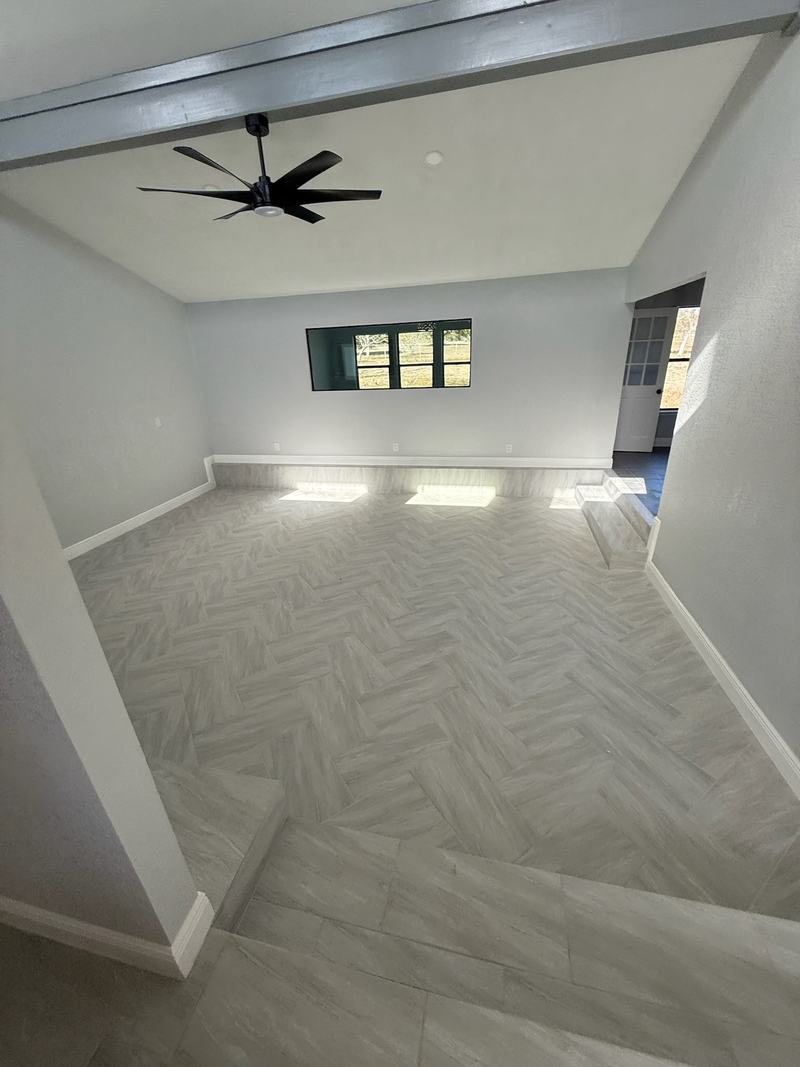 Bright room with a herringbone plank tile floor, a painted beam, a step-down and a ceiling fan