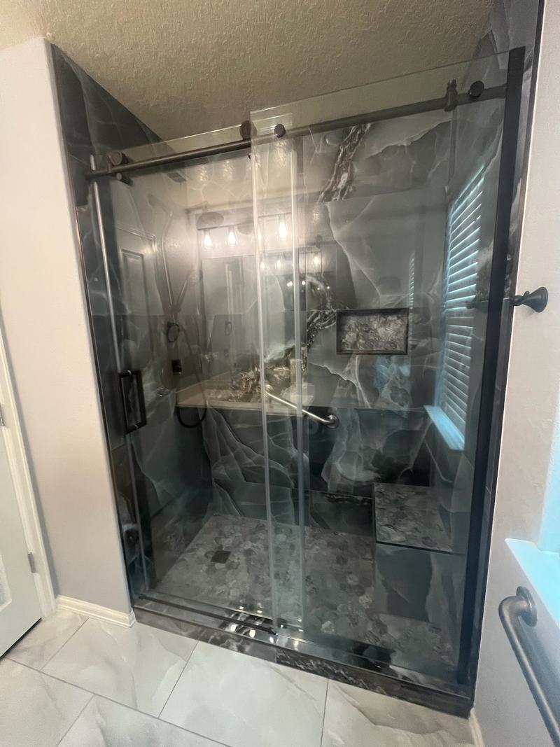 Walk-in shower with onyx-look tile, a niche, a tiled bench and bronze-framed sliding glass doors