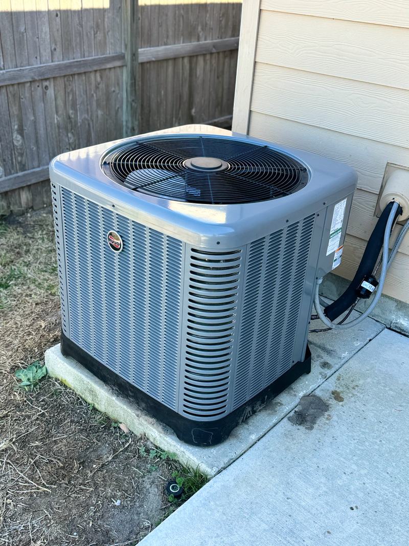 Gray outdoor air-conditioning condensing unit on a concrete pad beside the house, with an insulated refrigerant line set and electrical whip