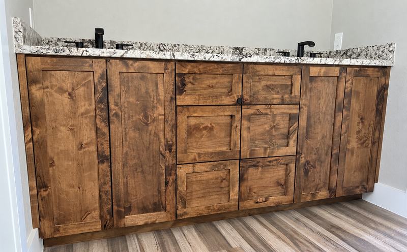Knotty alder double vanity with paired shaker doors, a center bank of drawers, a granite top and two black faucets