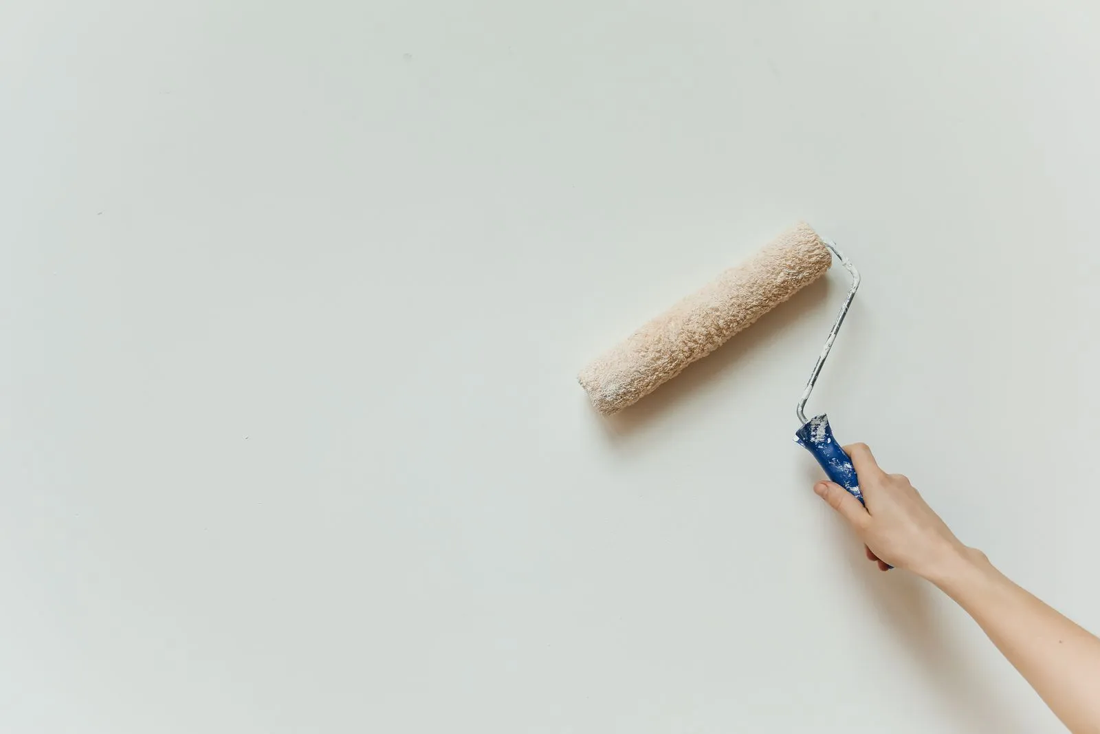 Hand rolling fresh white paint onto a smooth interior wall.